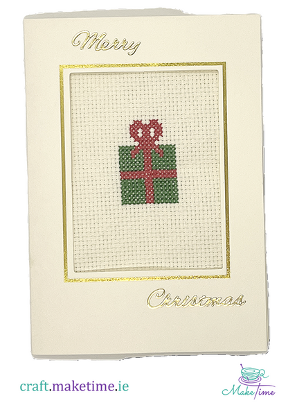 Cross-stitched Christmas gift box on a cream card with 'Merry Christmas' text.