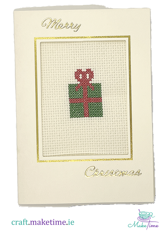 Cross-stitched Christmas gift box on a cream card with 'Merry Christmas' text.