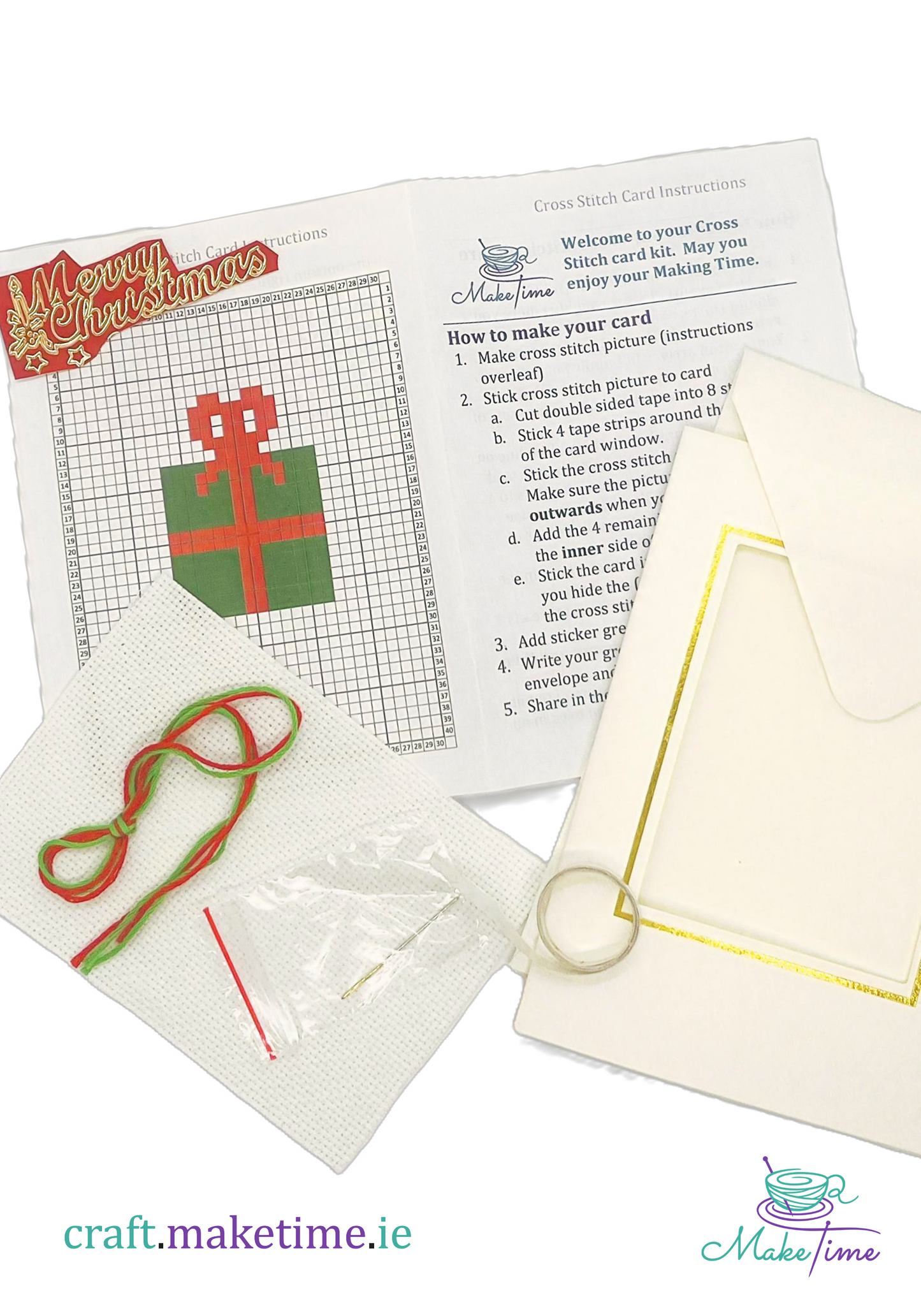 Cross stitch kit with Christmas gift pattern, needle, thread and white envelope on a white background.