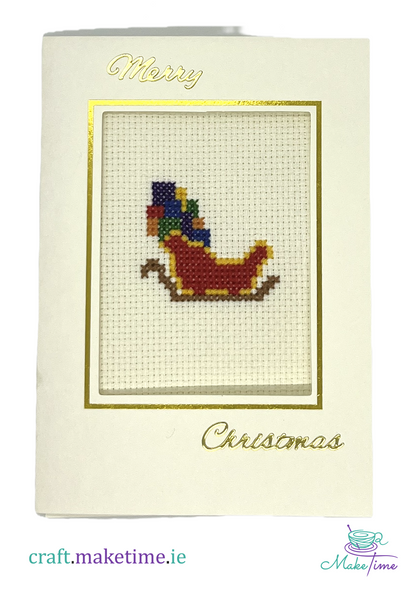 Cross-stitched Christmas card with a santa's sleigh full of presents design on a white background